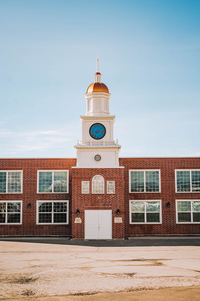 Sunlit clock tower on a vintage brick building under a clear blue sky.